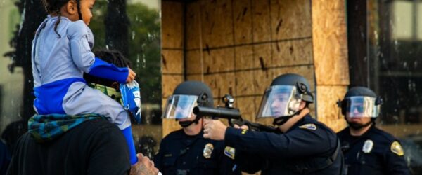 아이를 목마 태우고 있는 남자에게 총을 겨누는 미국 경찰, Photo by Richard Grand