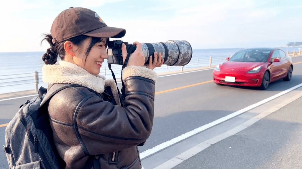달려오는 테슬라 자동차를 망원렌즈로 담고 있는 멋진 여성 사진가